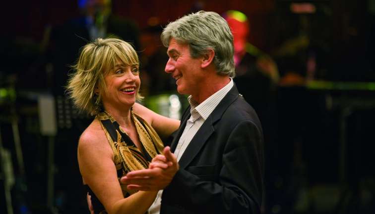 An older couple dancing, the man wearing a shirt and suit jacket