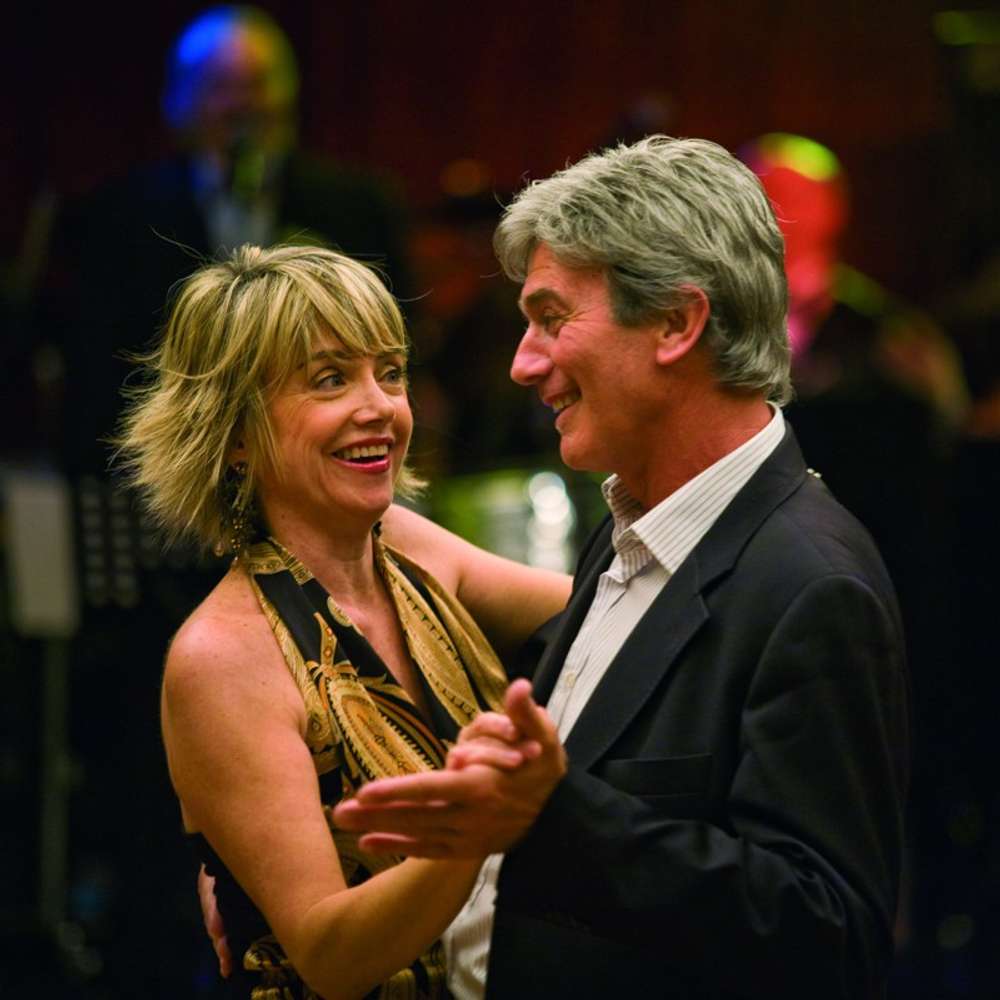 An older couple dancing, the man wearing a shirt and suit jacket