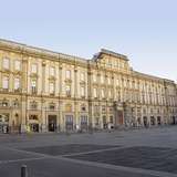 A wide palatial building opening onto a city square