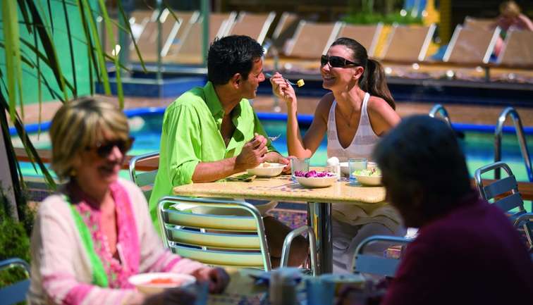 A younger couple enjoying breakfast outside, overlooking a pool area