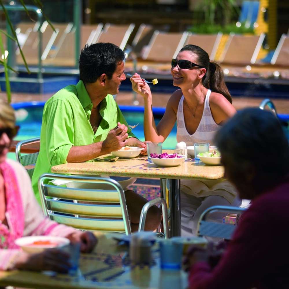 A younger couple enjoying breakfast outside, overlooking a pool area