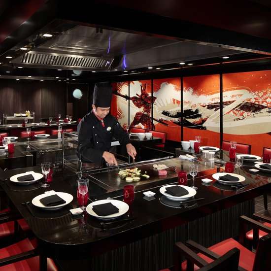 A chef in black preparing Japanese cuisine teppanyaki style