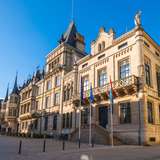 An elegant palace facade with several flags out front and a glass bridge on the side