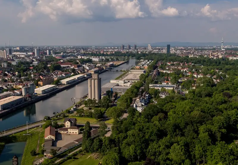 An image of Ludwigshafen from afar, with the river flowing and green trees in the foreground
