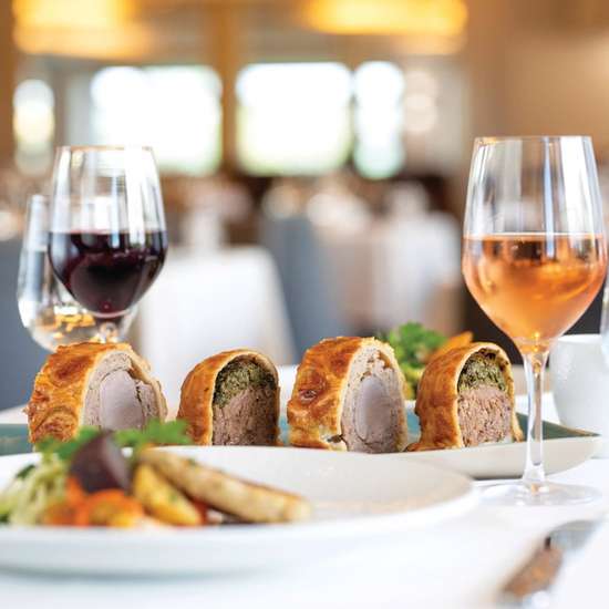 Glasses of wine and slices of an elevated beef wellington on a table in a fine gastropub