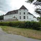 A white-walled castle with a round tower and grey tiled roofing