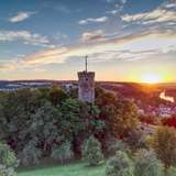 An image of a castle rampart towering above a cluster of trees at sunset