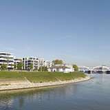 A riverside promenade with a grassy bank and modern mansions in the background