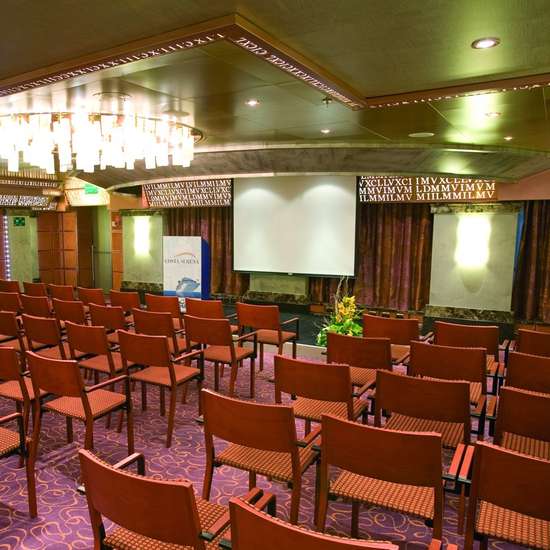 Rows of orange chairs in a meeting room, in front of a projector screen