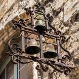 An iron sign on the side of an old building featuring three bells