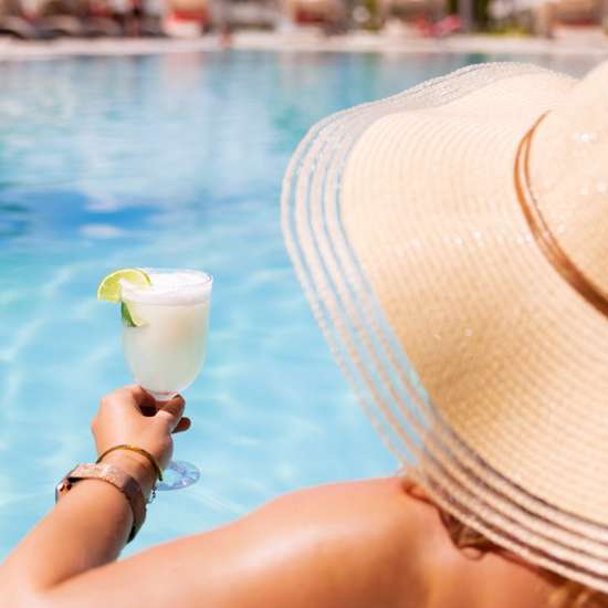 A woman in a sunhat enjoying a cocktail poolside