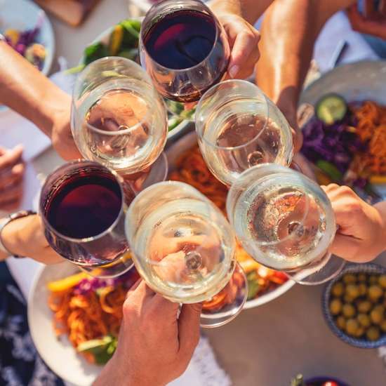 A top-down look at several hands clinking wine glasses over Mediterranean food